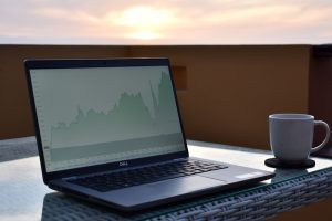 A laptop displaying a financial chart outdoors with a coffee mug nearby