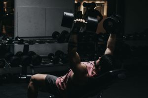 Muscular man in sportswear performing dumbbell bench press in a dimly lit gym setting. — Considering buying a treadmill for i