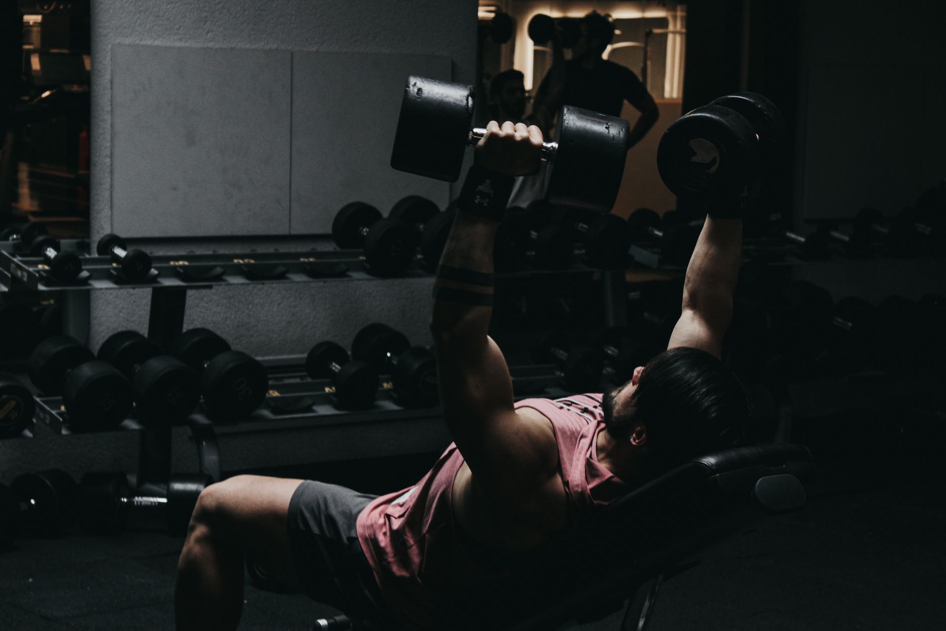 Muscular man in sportswear performing dumbbell bench press in a dimly lit gym setting. — Considering buying a treadmill for i