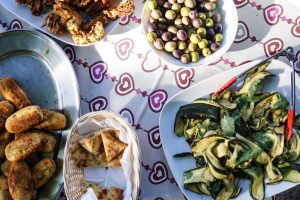 A vibrant top view photo of Mediterranean dishes including olives, zucchini, and various fried delicacies on a decorative tab